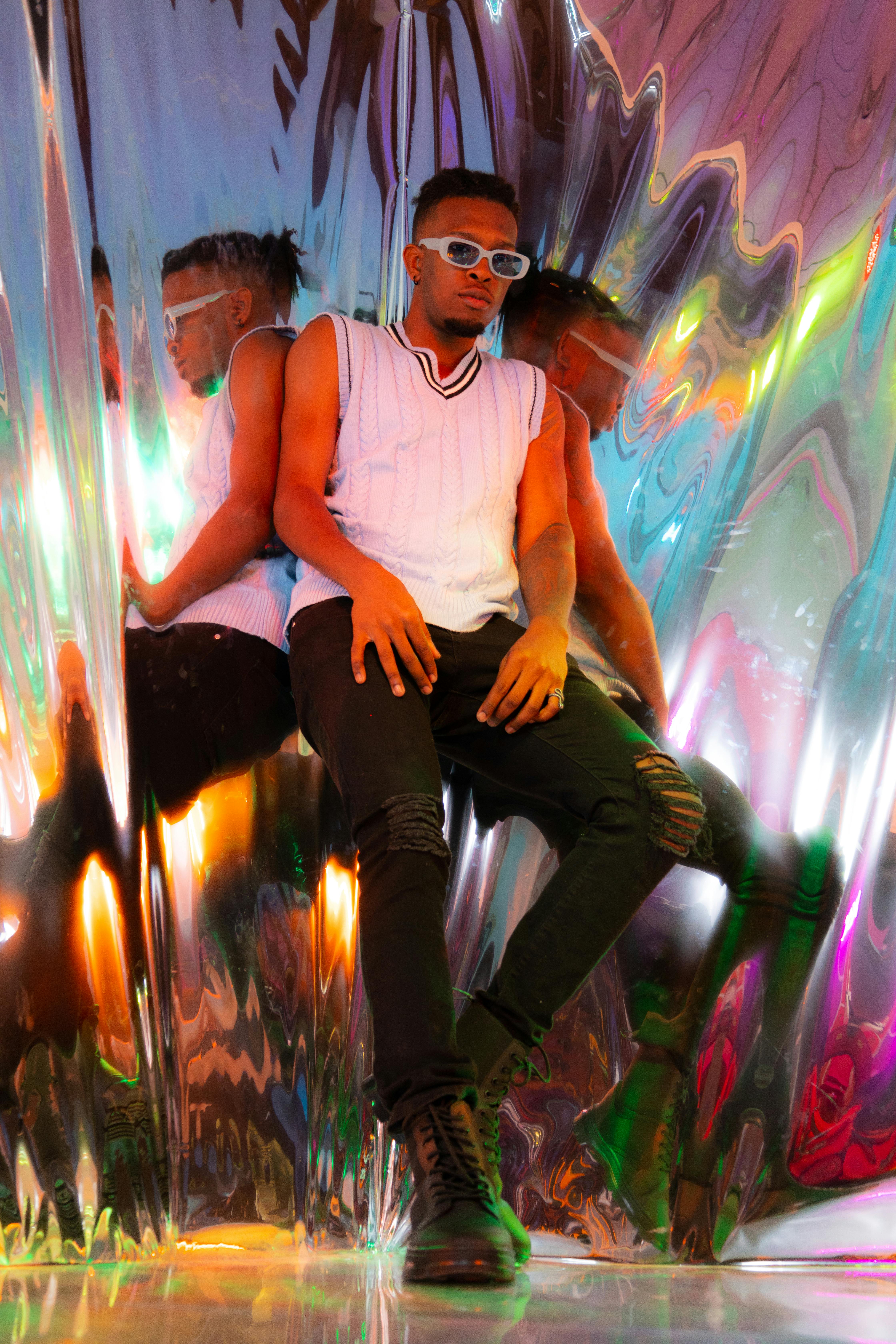 Trendy man in reflective setting with sunglasses and stylish attire.