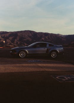 A sleek, parked car in a scenic countryside with mountain views at sunset.
