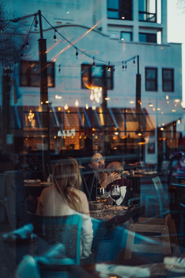 People In Restaurant Seen Through Window Reflecting City Street