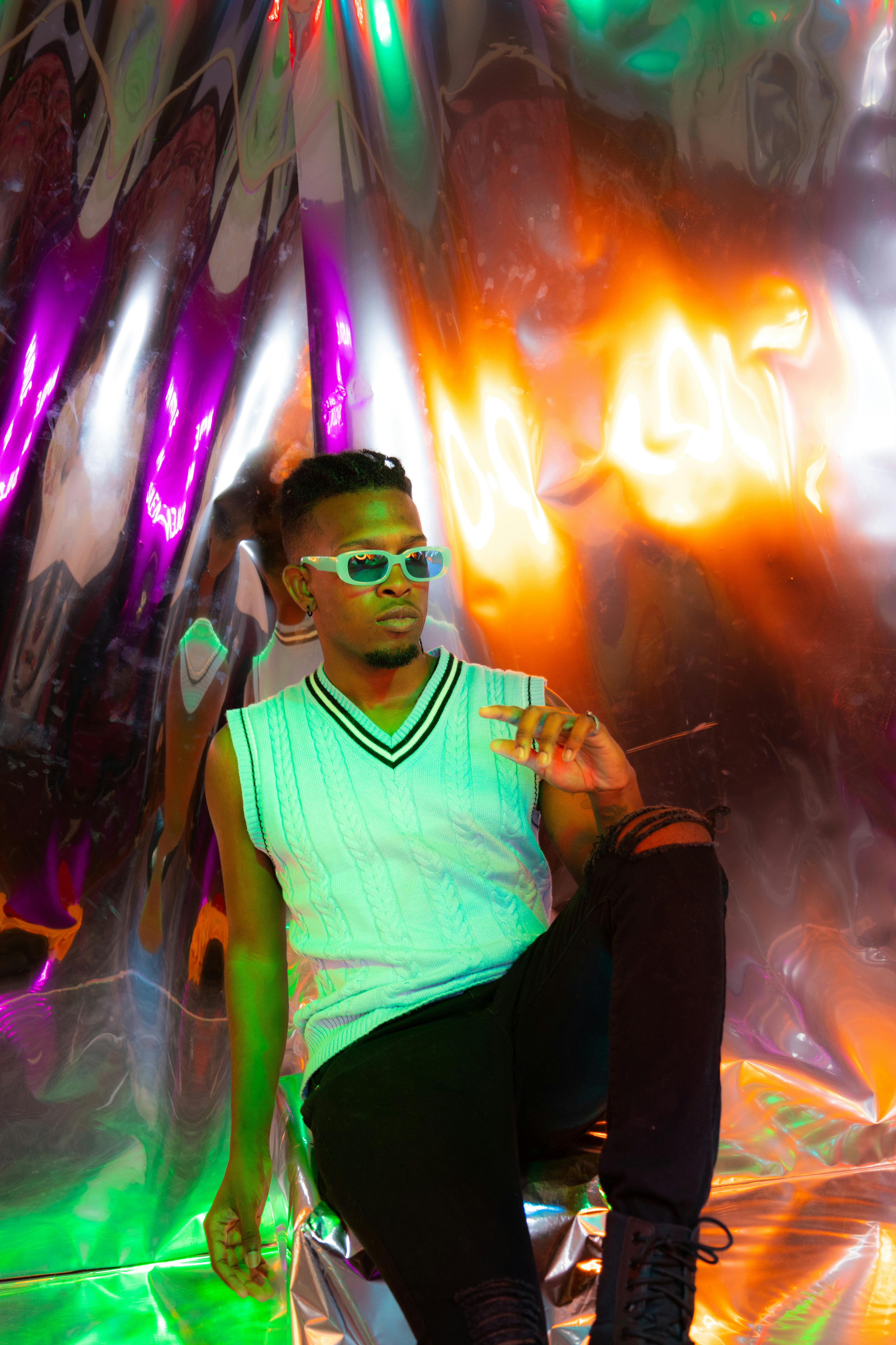 Fashionable man in sunglasses posing against a colorful reflective backdrop, showcasing modern style.