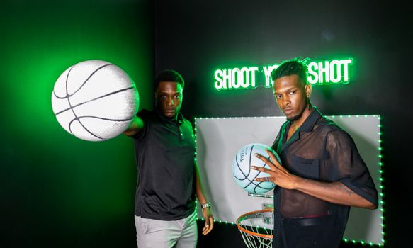 Two men posing with basketballs in a neon-lit studio, showcasing modern sports fashion.