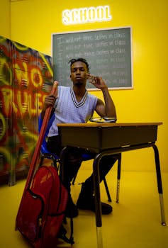 A young man sitting in a classroom with vibrant decor and a humorous chalkboard message.