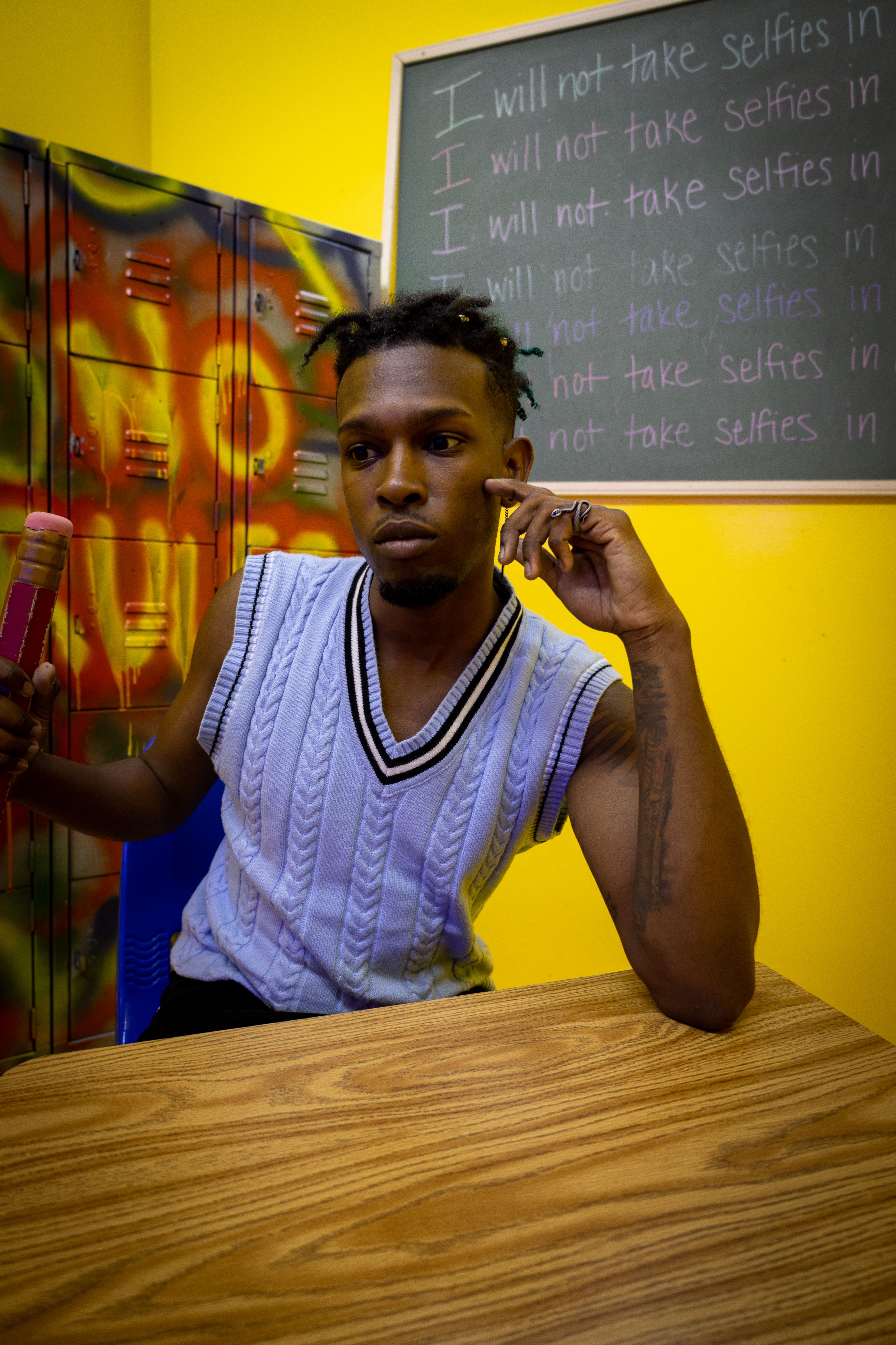 Man seated indoors with chalkboard and colorful graffiti lockers in a classroom setting.