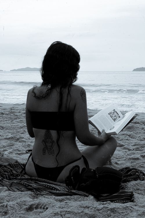 Free A woman in a swimsuit reading a book on Ubatuba beach, Brazil, enjoying the summer vibes. Stock Photo