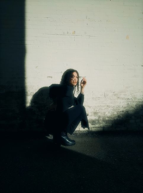 Model crouching against a white wall with striking shadows in an urban setting.