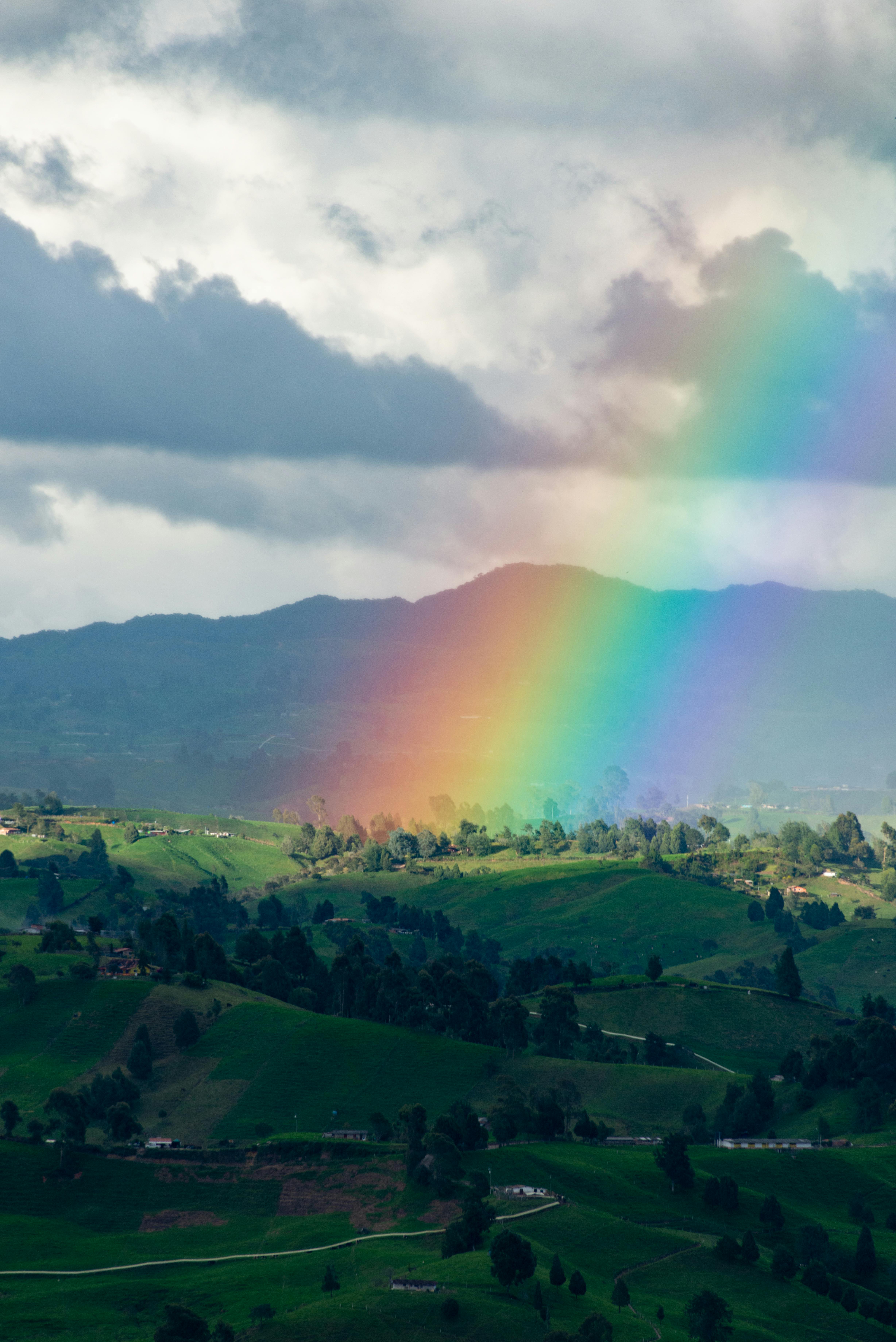 Colorful rainbow arcs over lush green hills and cloudy sky, capturing natural beauty.