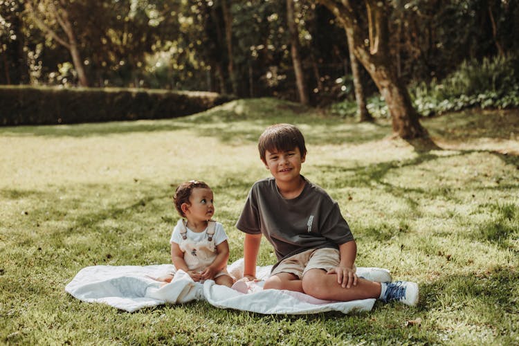 Photo Of A Boy And A Baby Sitting On A Blanket In The Park