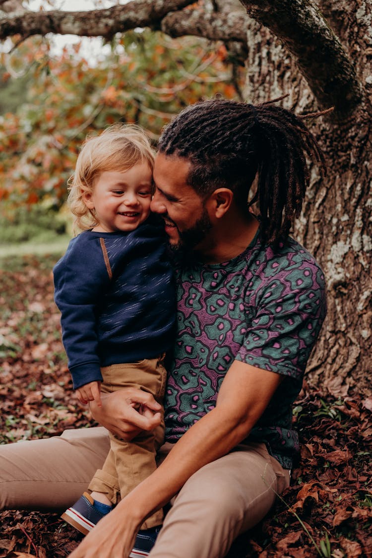 Photo Of A Man With A Baby Boy Sitting Under A Tree