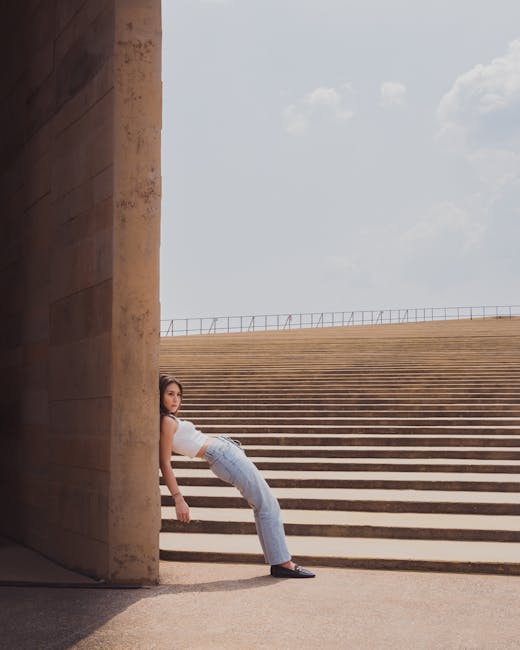 A fashionable young woman in a white tank top and jeans poses against a modern urban staircase in Mexico City.