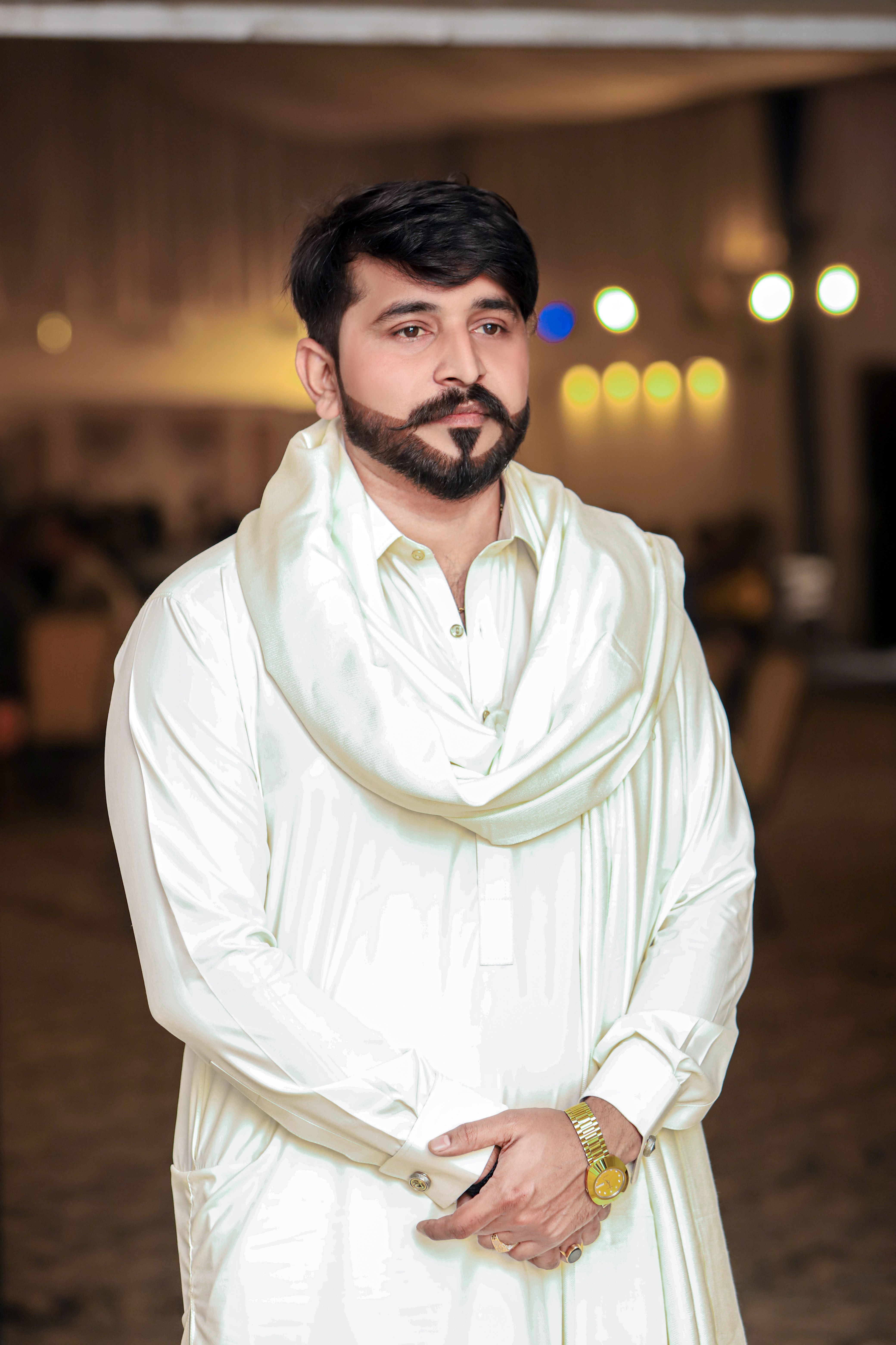 Portrait of a man in traditional attire, elegantly posing indoors with a warm and neutral backdrop.
