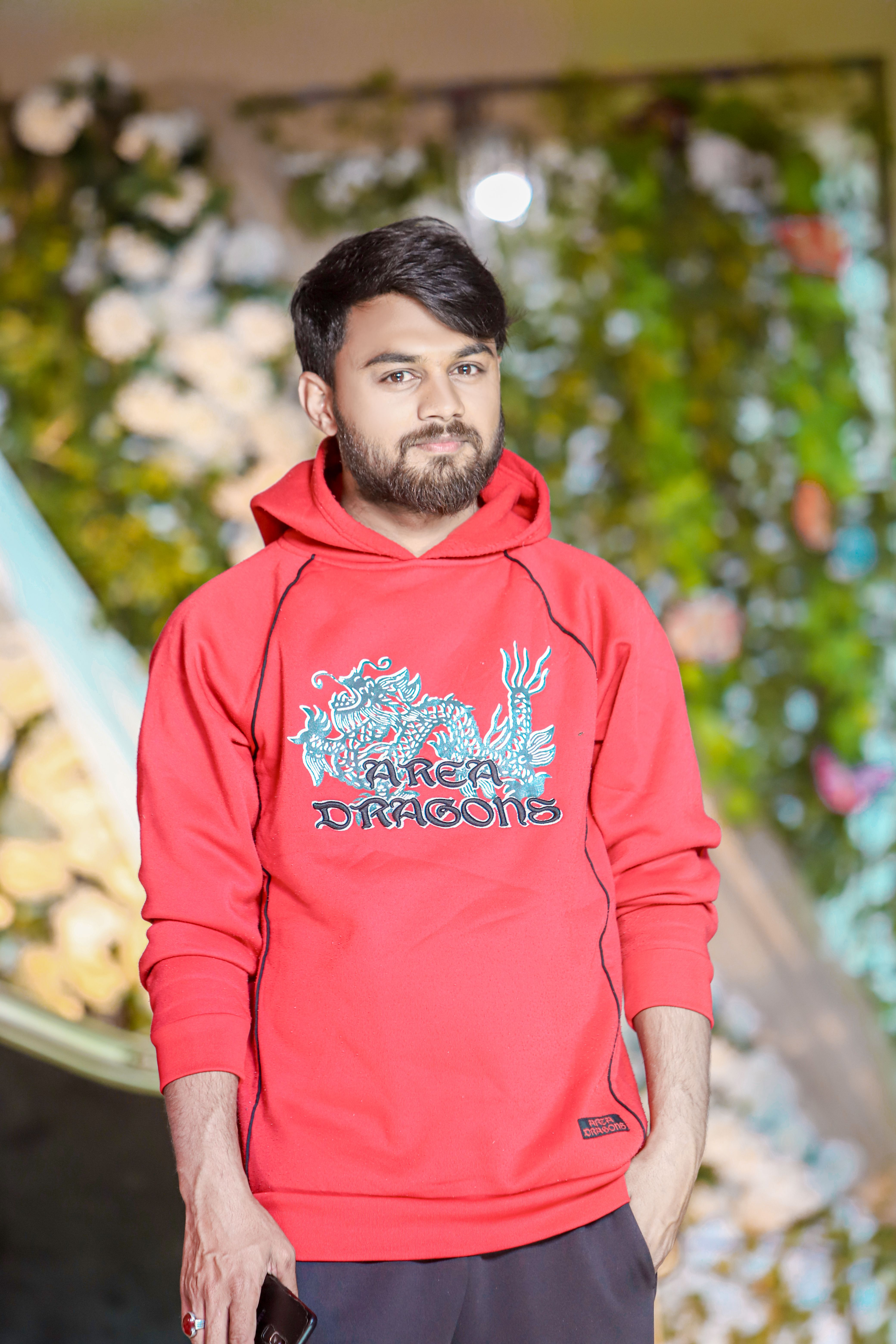 Portrait of a young man in a red hoodie with a dragon design, smiling outdoors.