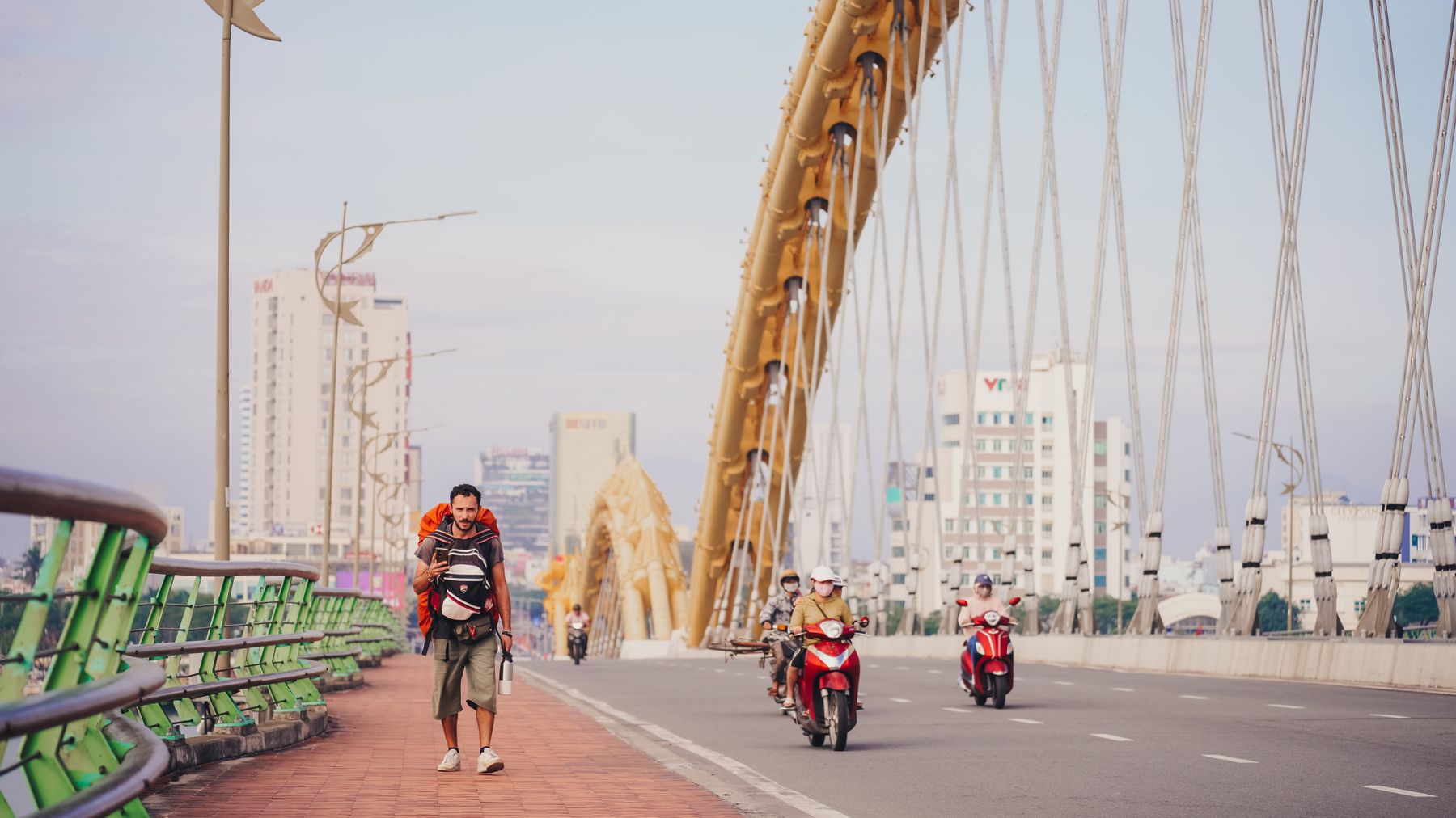 A man walking on the Dragon Bridge in Da Nang with motorbikes passing. Urban scene with city buildings.
