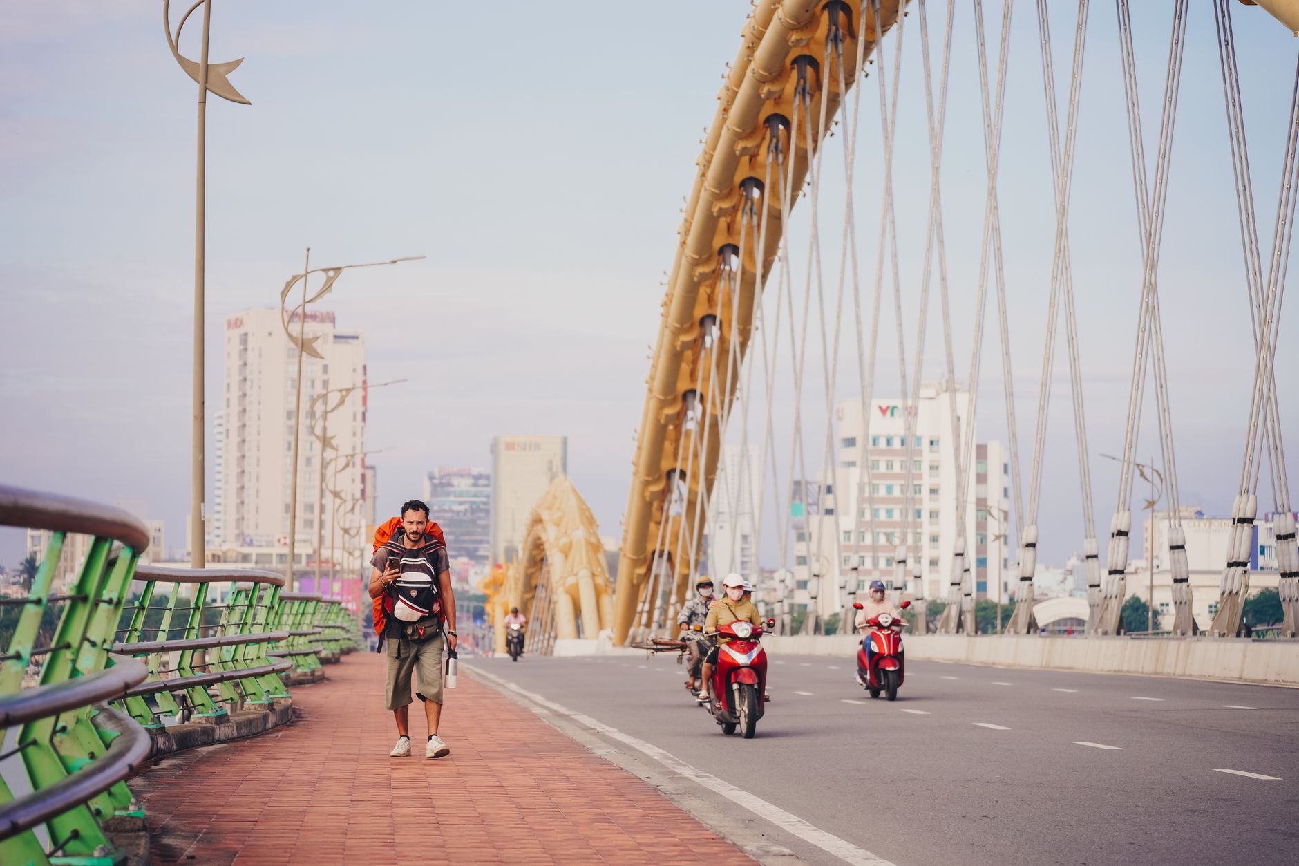 A man walking on the Dragon Bridge in Da Nang with motorbikes passing. Urban scene with city buildings.