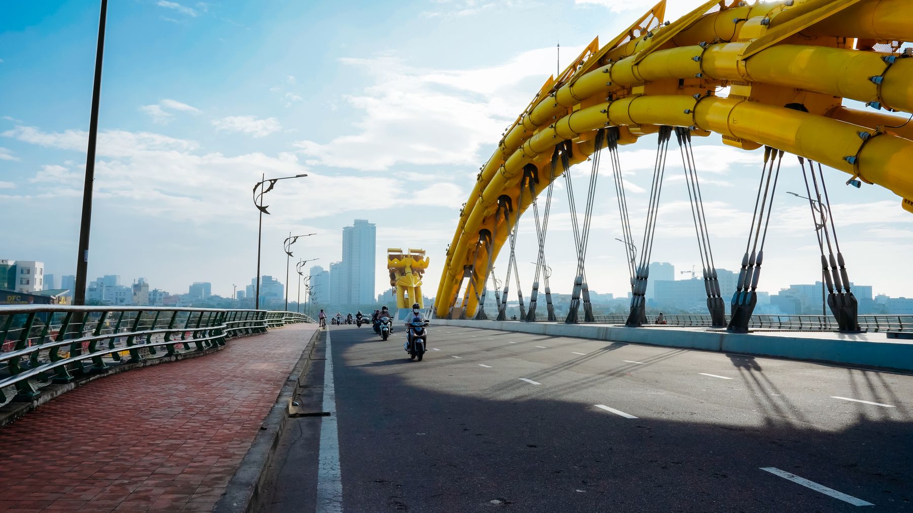 Motorcycles cross the iconic yellow Dragon Bridge in Da Nang under a clear blue sky.
