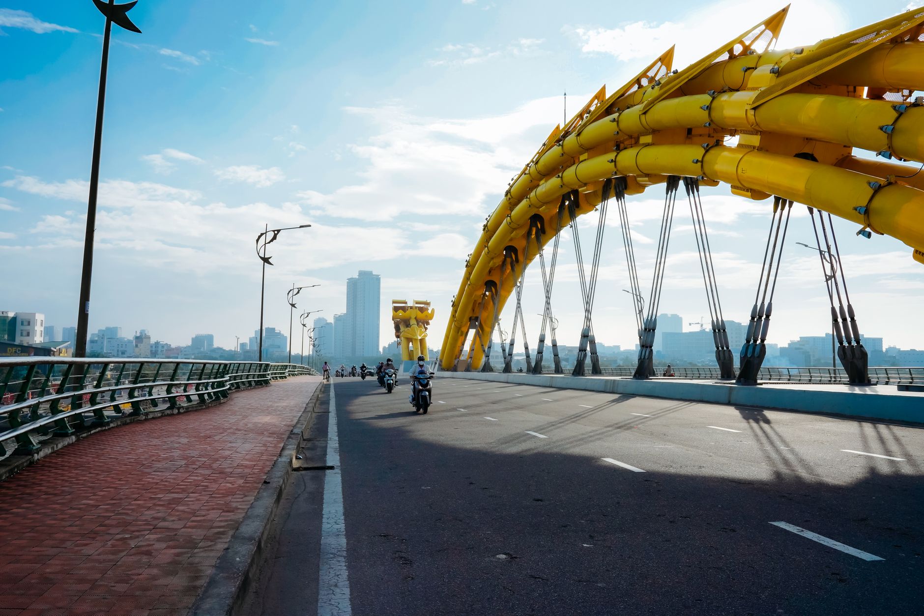 Motorcycles cross the iconic yellow Dragon Bridge in Da Nang under a clear blue sky.