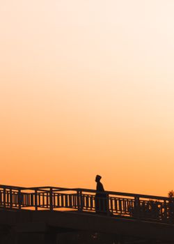 A dramatic silhouette of a person walking on a bridge against an orange sunset sky in Kaduna, Nigeria.. pexels, dramatic, sil