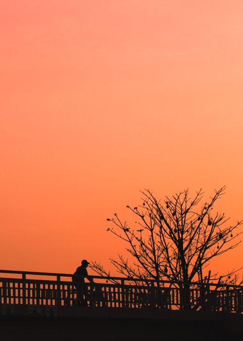 Free A lone biker rides across a bridge silhouetted by a vibrant orange sunset in Kaduna, Nigeria. Stock Photo