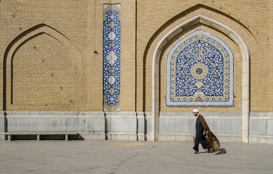Middle-Eastern man walking past a beautifully decorated mosque wall in Qom, Iran.