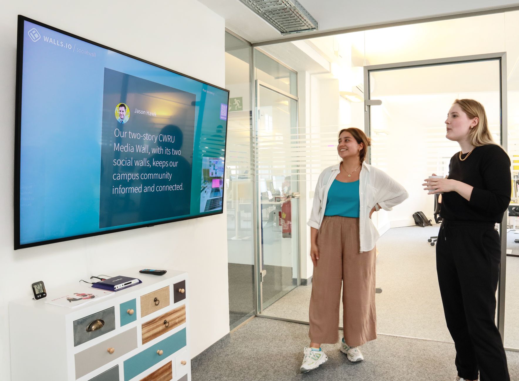 Two women engaged in a collaborative discussion in a modern office setting with a large display screen.