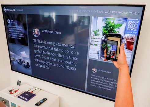 A person uses a smartphone to scan a QR code displayed on a large screen indoors.