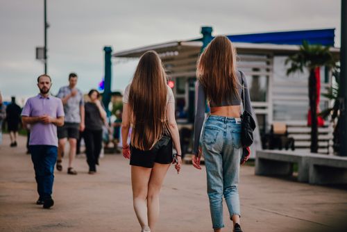 Free Two women walking on a city street with long hair, wearing casual summer outfits. Stock Photo