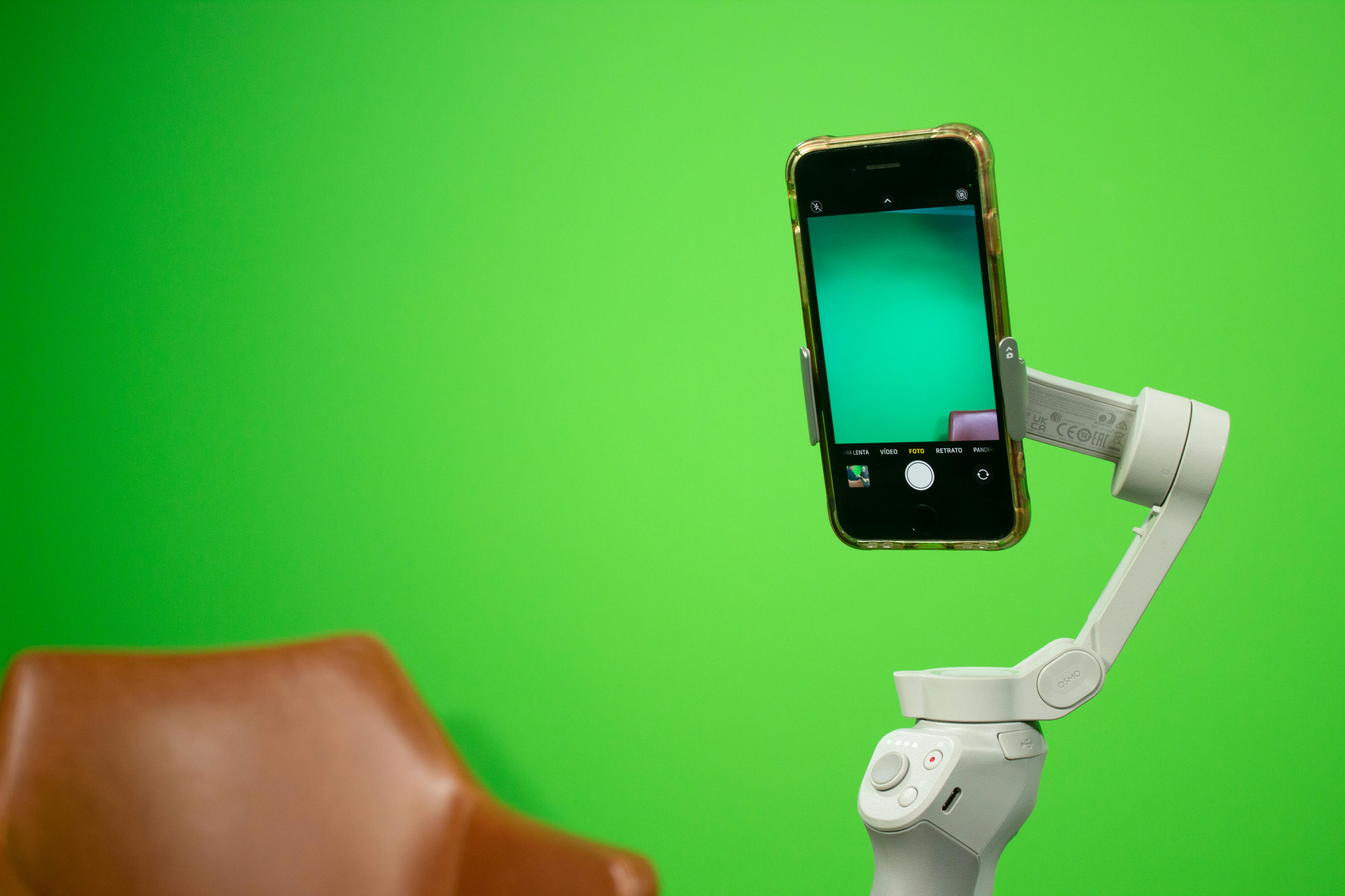 Smartphone mounted on a stabilizer in front of a green screen setup for video production.