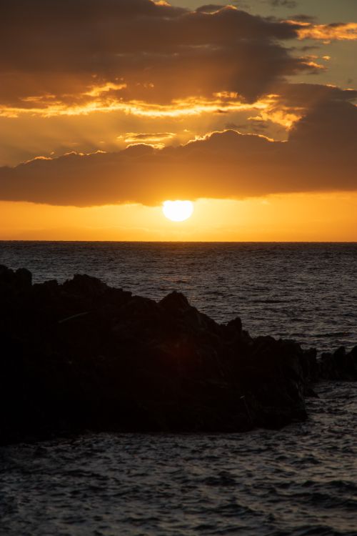 Free A stunning coastal sunset casting a warm glow over the ocean horizon with silhouetted cliffs. Stock Photo