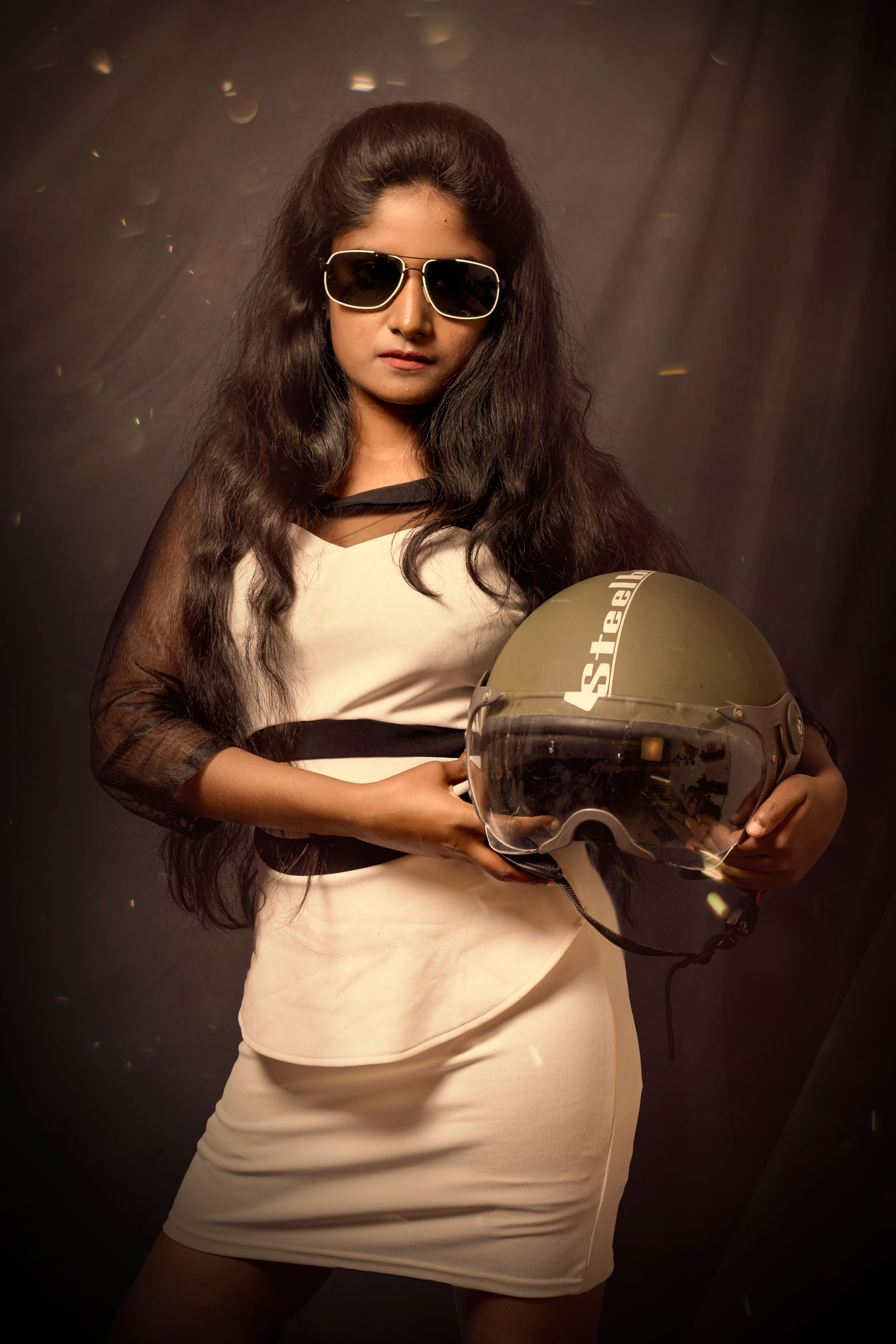 Chic woman in white dress and sunglasses holding a helmet in a studio setting.