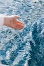 一只手触摸清澈的蓝色海水的特写，创造出美丽的涟漪，唤起一种宁静的感觉