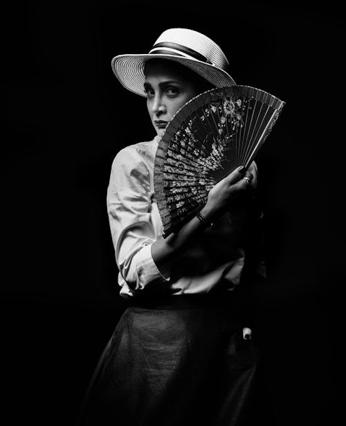Black and White Photo of a Woman in a Hat Holding a Fabric Fan 