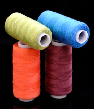Close-up of colorful sewing threads against a black background in a vertical shot.