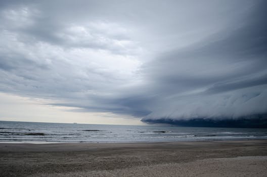 Dark storm clouds form over a deserted beach, creating a dramatic seascape.