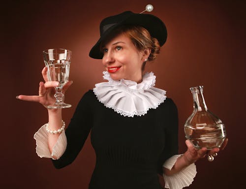 Elegant Woman in a Black Hat and Dress Holding a Bottle and Glass 
