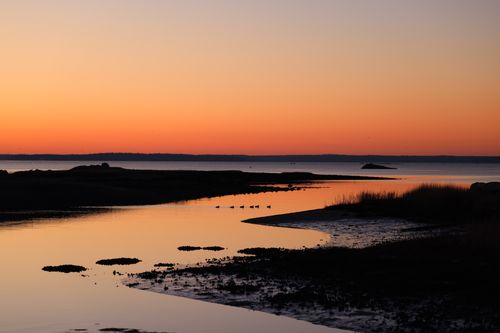 Free Serene coastal sunset with vibrant orange hues reflecting on the tranquil sea. Stock Photo