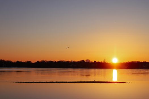 Tranquil sunrise over calm waters in Stamford, Connecticut, with vibrant colors reflecting on the surface.