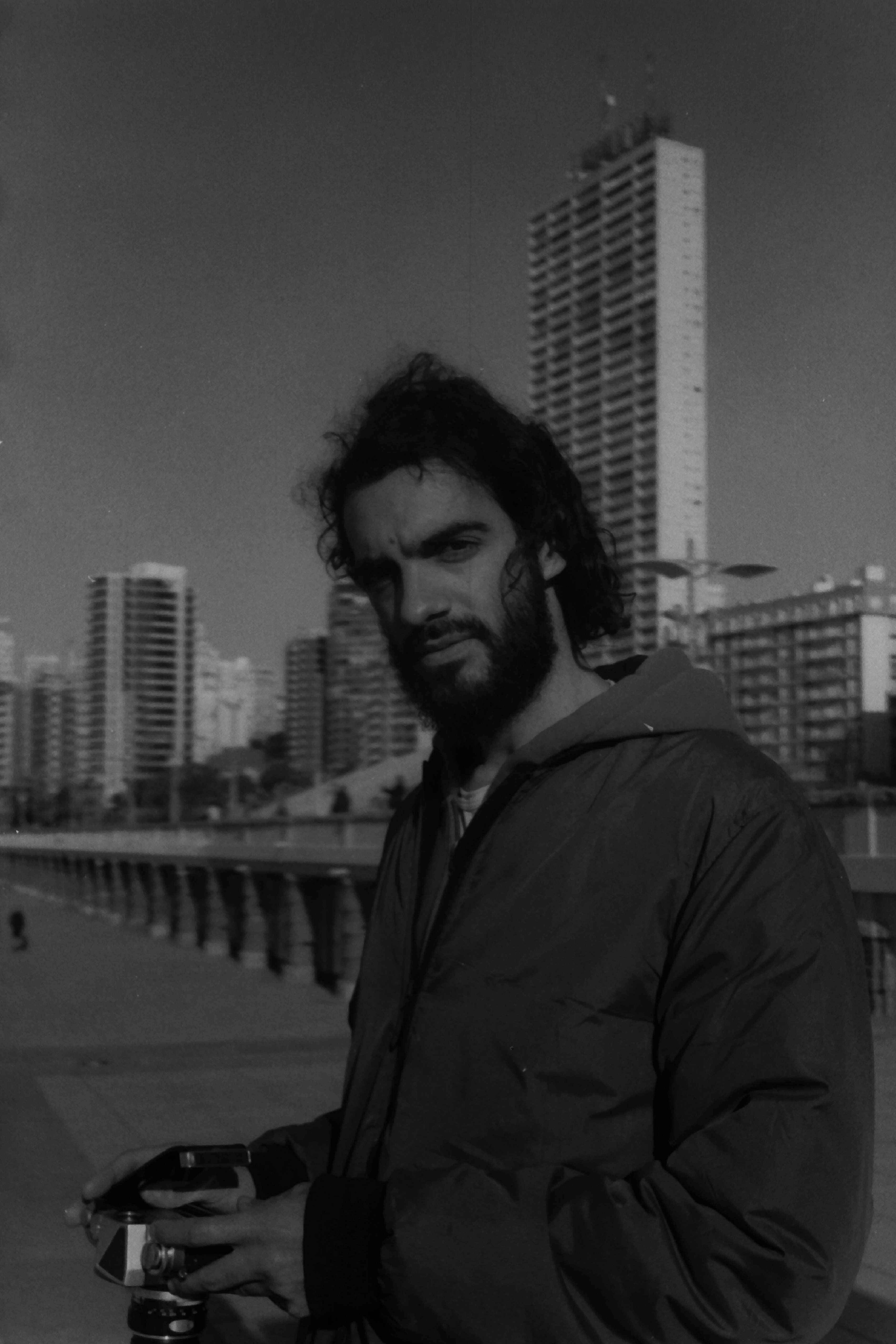 Moody black and white portrait of a bearded photographer in a cityscape backdrop with skyscrapers.