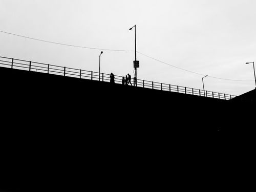 Free Silhouette of people walking on an urban bridge under a cloudy sky. Stock Photo