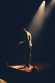 A singer stands on stage under a dramatic spotlight, creating a moody atmosphere.