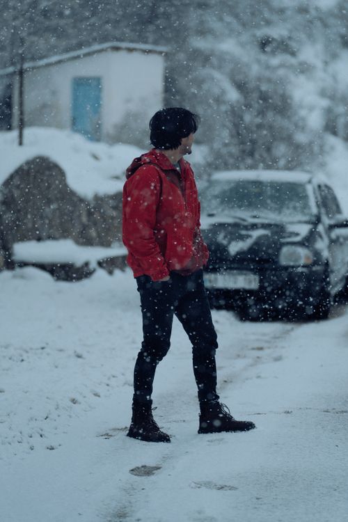 Free A man in a red jacket walks through a snowy urban setting during winter, showcasing the seasonal ambiance. Stock Photo