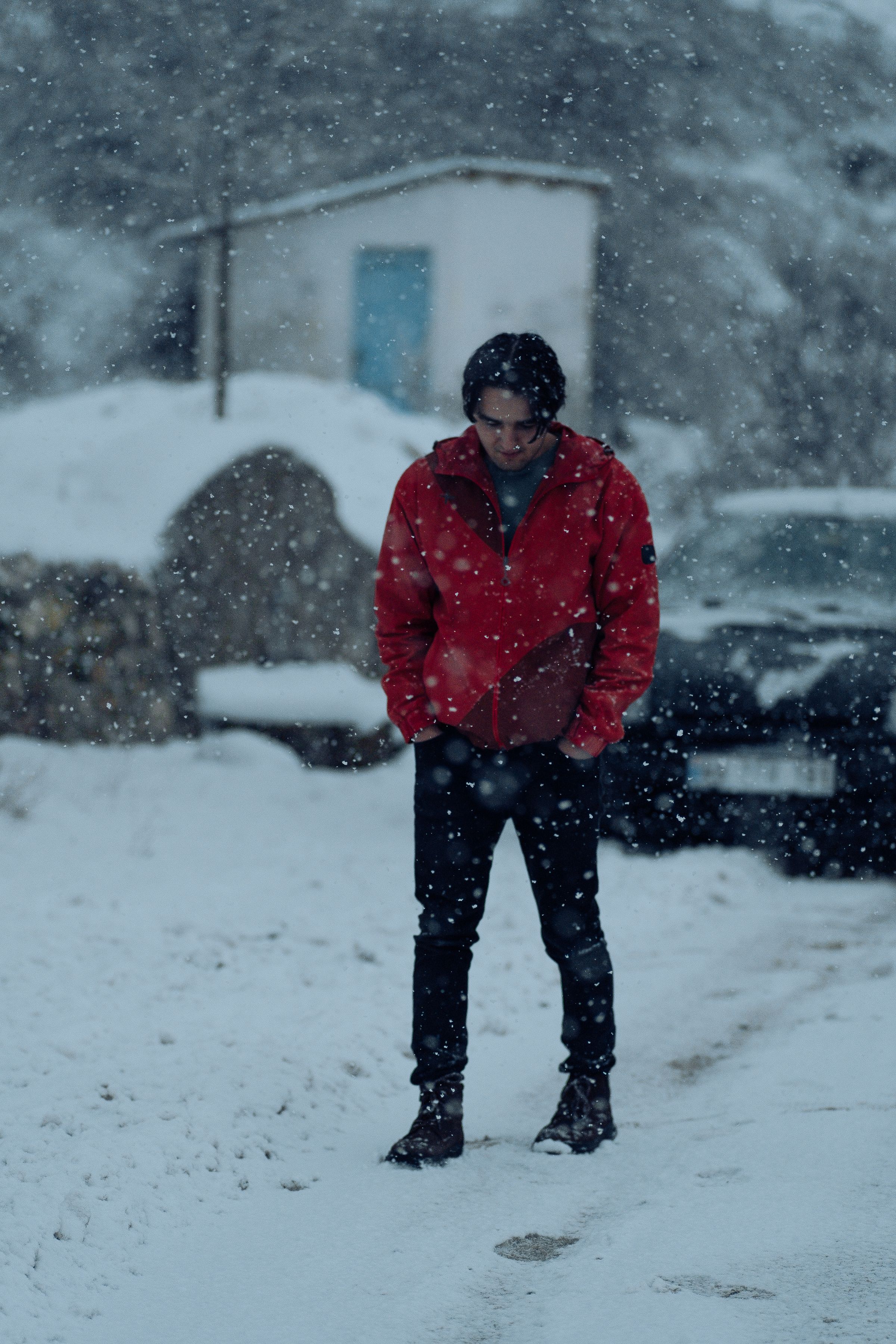 Man in red insulated jacket walking through falling snow in cold weather