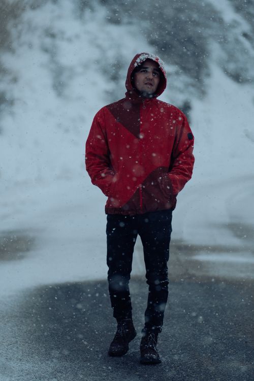 Free Person in a red jacket stands amidst falling snow, creating a moody winter scene. Stock Photo