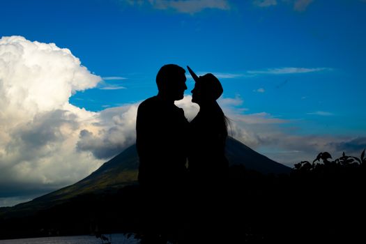 Silhouette of a couple standing together with a mountain backdrop and dramatic sky.