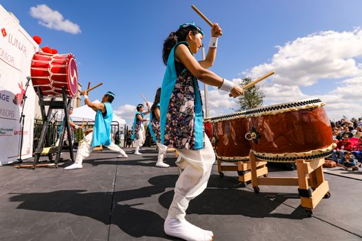 A group performing an energetic Taiko drum show outdoors at a lively cultural festival.