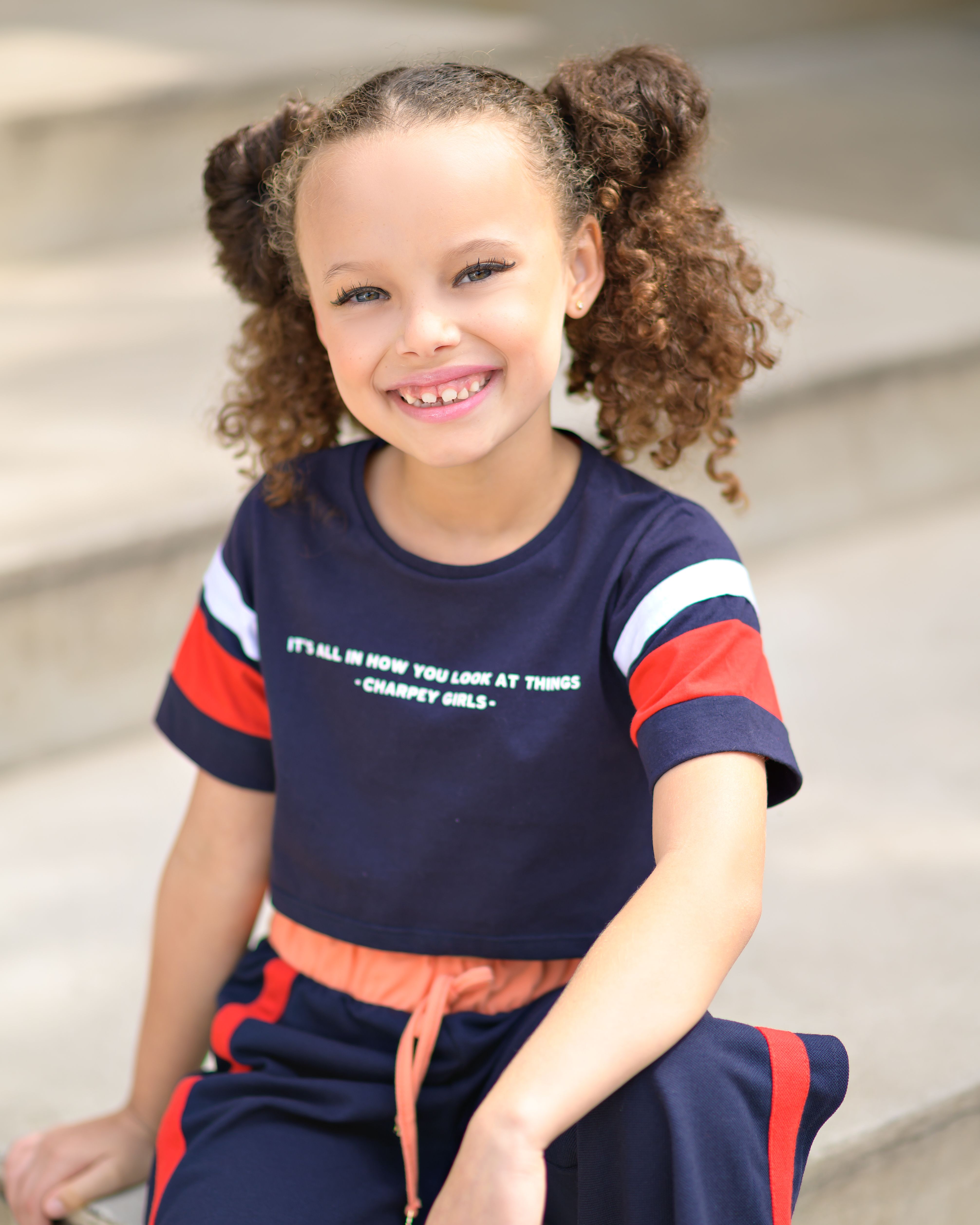 Happy teenager with curly hair in casual clothing smiling on outdoor steps.