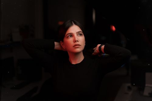 Free Thoughtful woman in a dark setting, wearing black clothes, adjusting her hair. Stock Photo