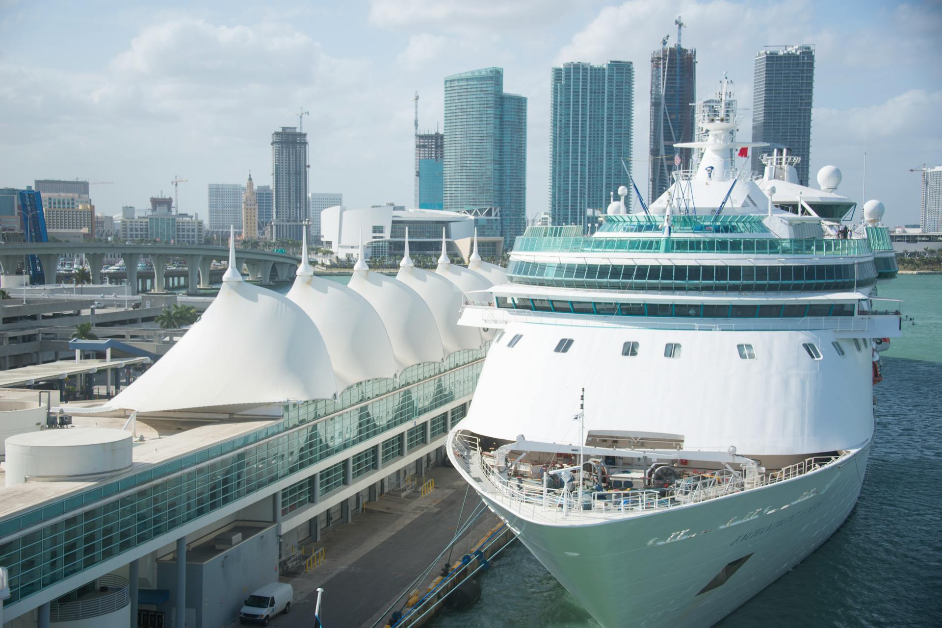 Luxury cruise ship docked at Miami harbor with city skyline in the background.