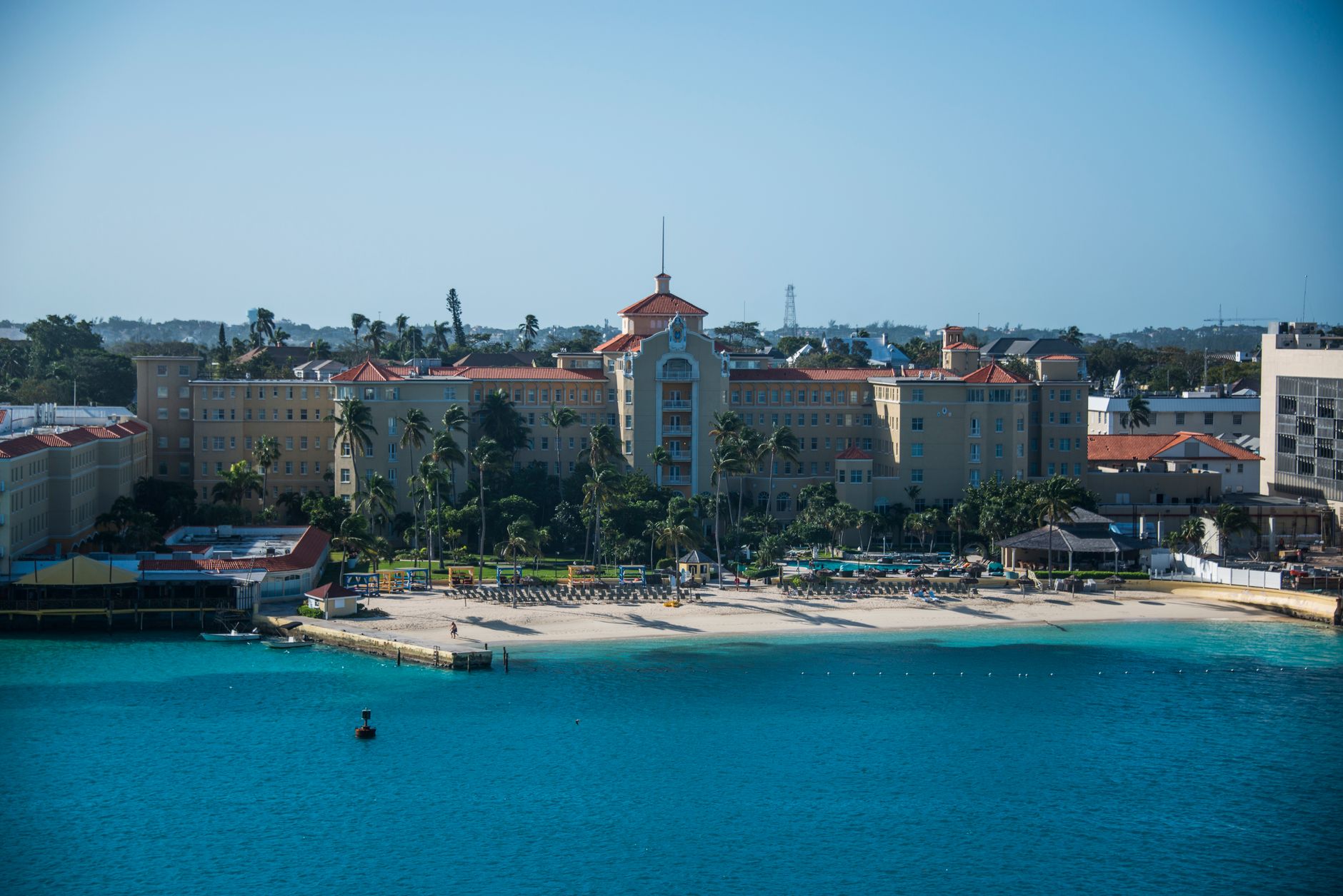 Scenic aerial view of a luxurious hotel by a beautiful turquoise beach under a clear blue sky.
