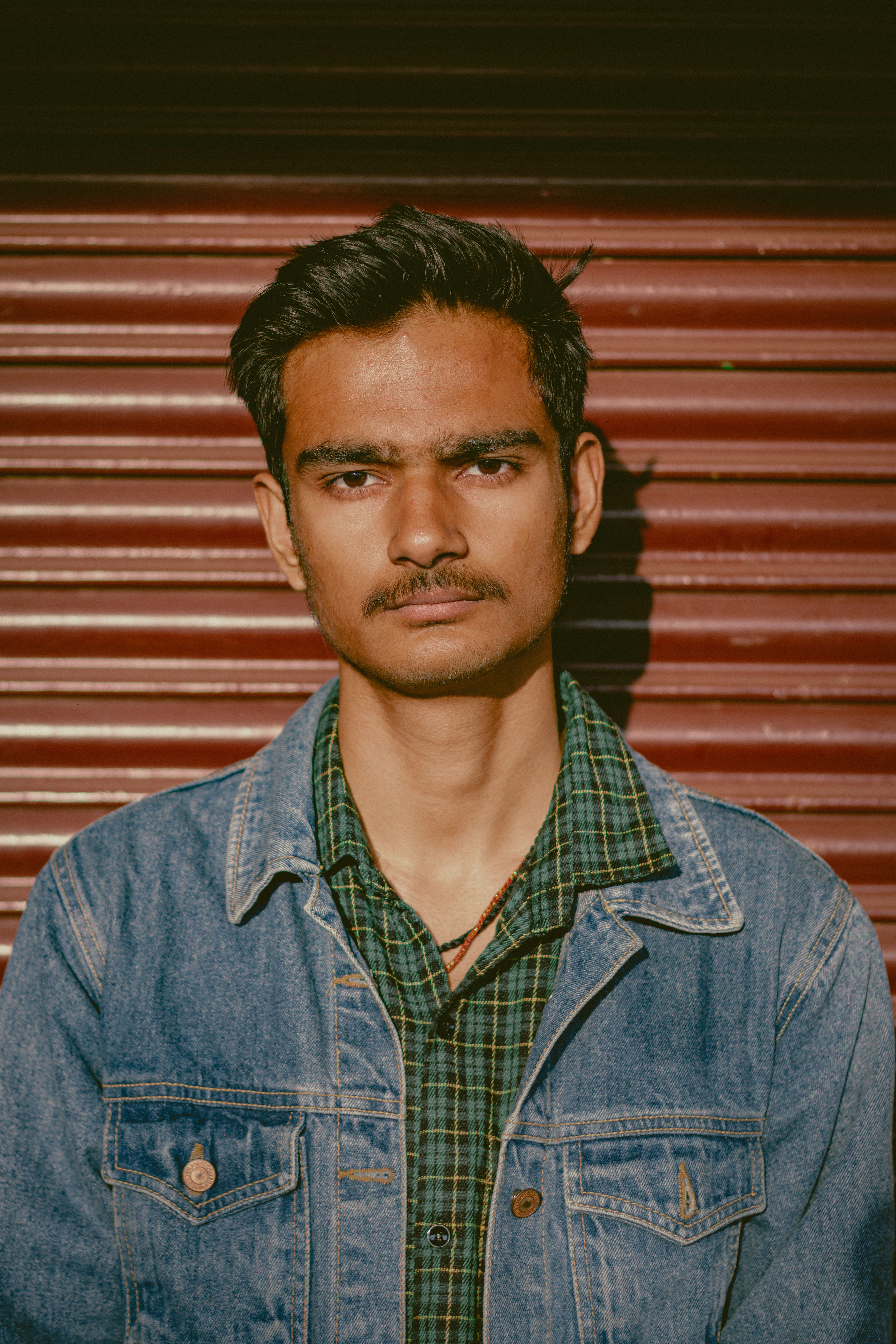 Close-up portrait of a young man in a denim jacket against a red shutter background. Perfect for lifestyle themes.
