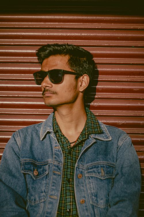 Free Portrait of a young man with sunglasses and denim jacket against a striped shutter background. Stock Photo