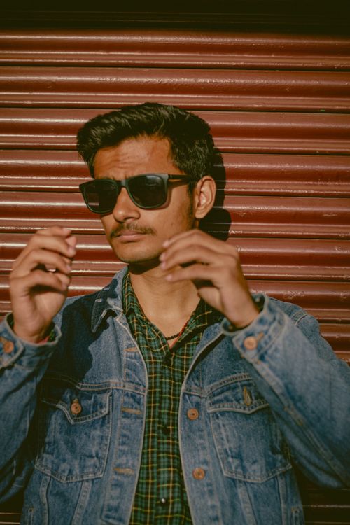 Free Young man wearing denim jacket and sunglasses with a confident pose outdoors. Stock Photo